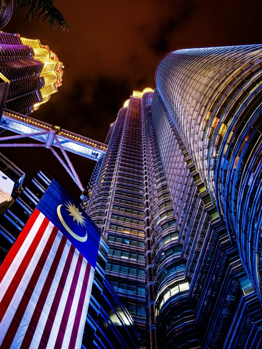 Top 5 Places to Visit in Malaysia Dramatic view of Petronas Twin Towers illuminated at night with the Malaysian flag.